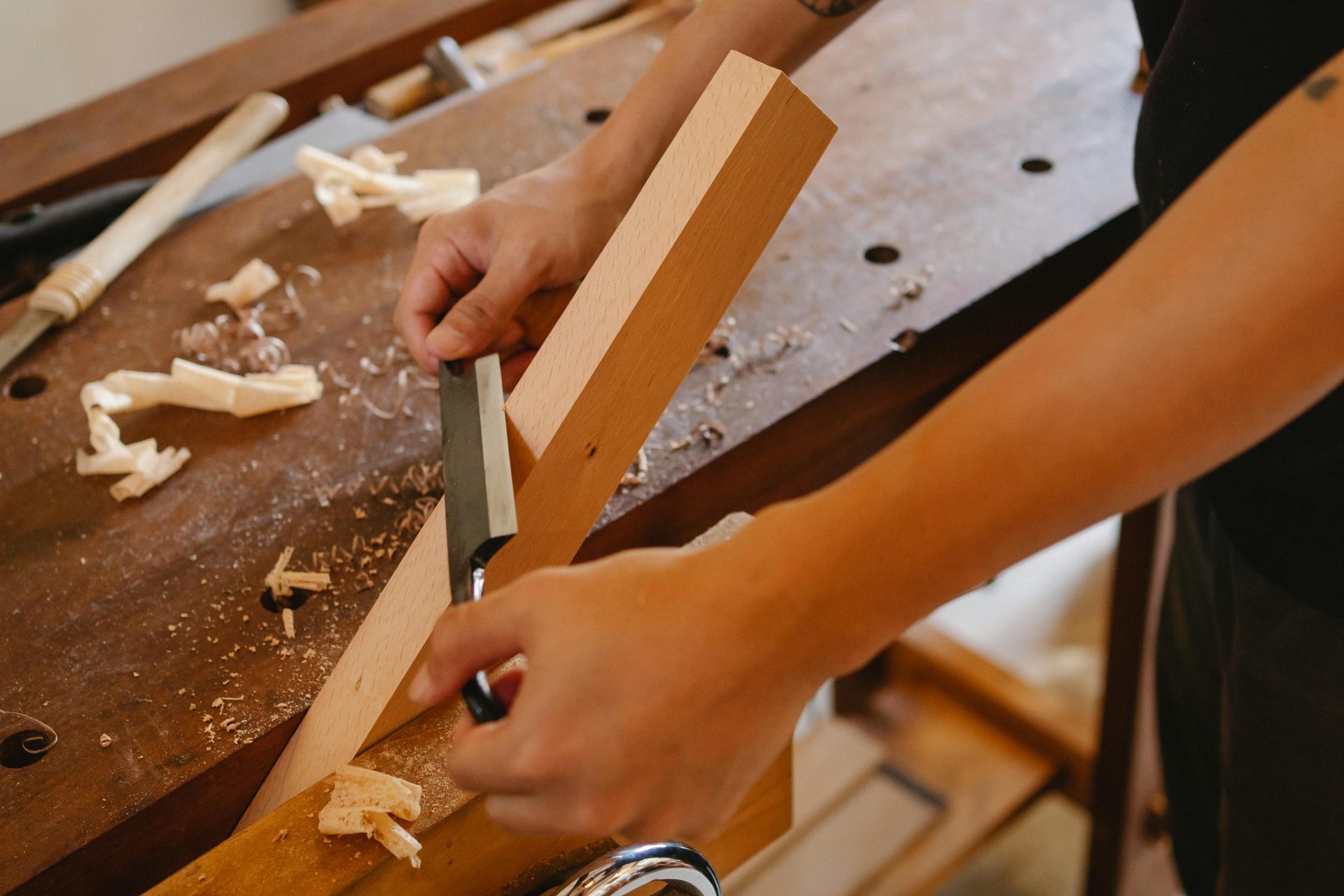A skilled craftsman using a chisel to carve wood in a busy workshop.
